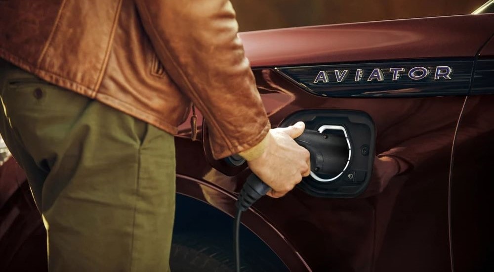 Close-up of someone plugging in a bronze 2023 Lincoln Aviator GT PHEV at a Lincoln dealer near Queens.