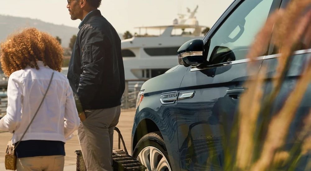 A couple with a picnic basket walking away from a blue 2023 Lincoln Navigator parked at a dock.