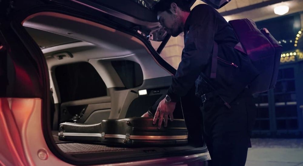 A man stowing an instrument case in a silver 2023 Lincoln Corsair at a Lincoln dealer near Queens.