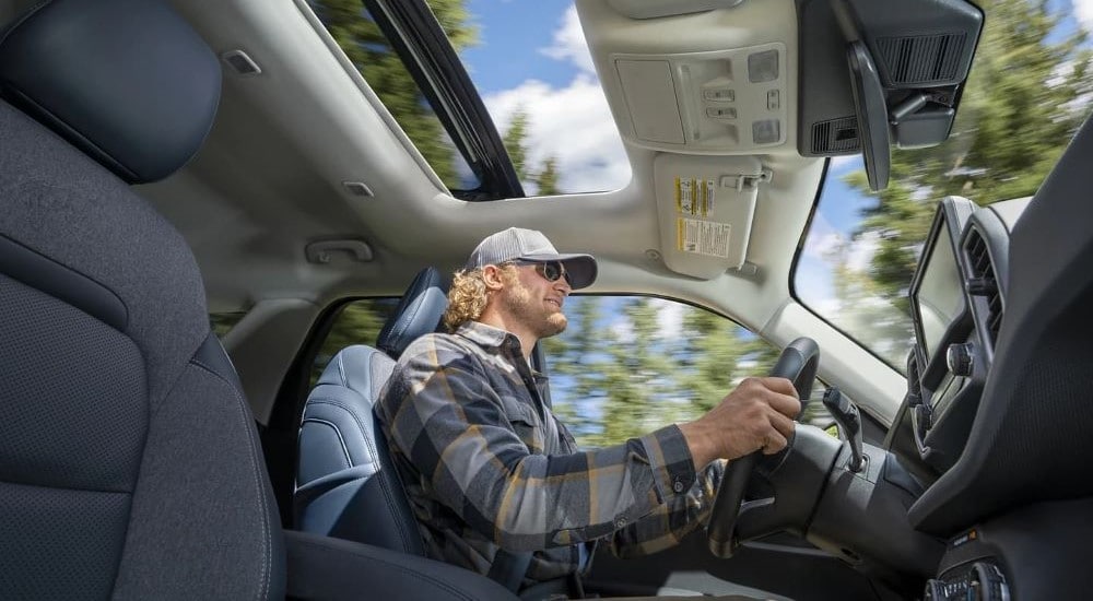 A man in a baseball cap and flannel shirt driving a 2022 Ford Bronco Sport to a Ford Dealer