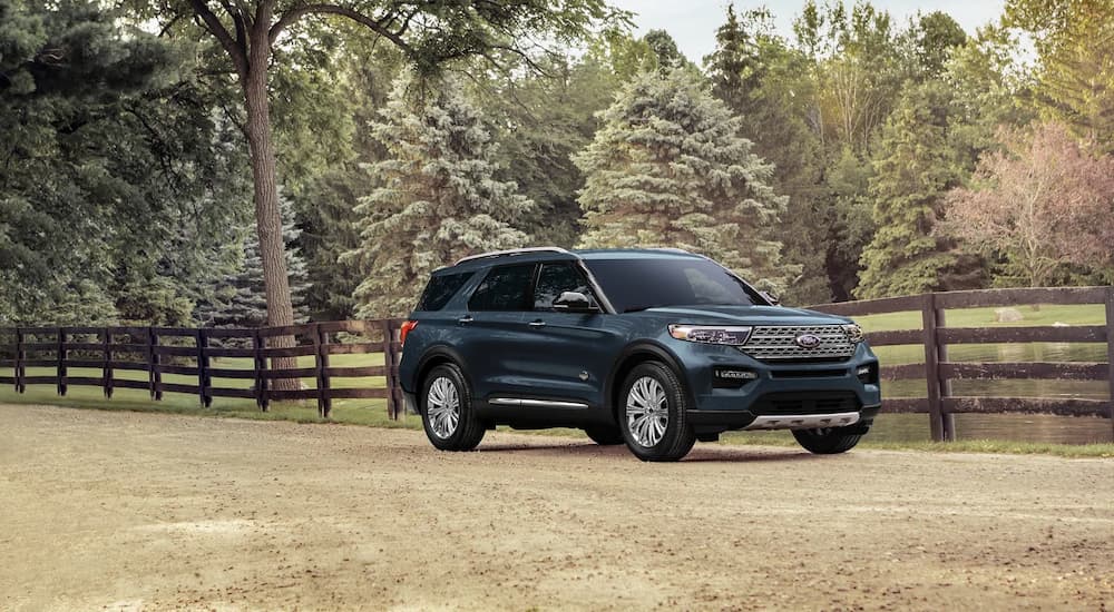 A blue 2023 Ford Explorer King Ranch parked in front of a wooden fence.