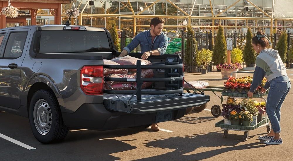 People loading items from a garden center into the bed of a black 2024 Ford Maverick