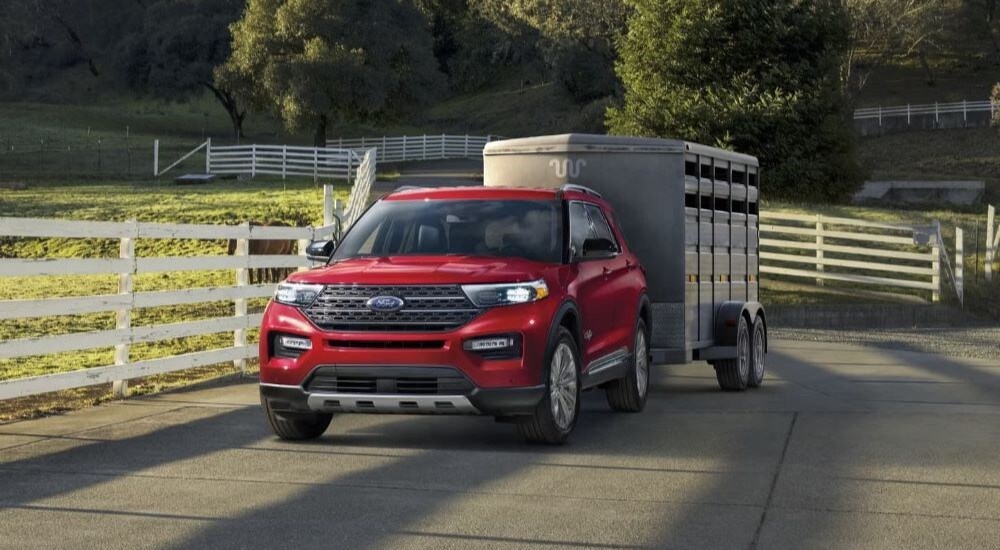 A red 2022 Ford Explorer King Ranch towing a trailer through a farm.
