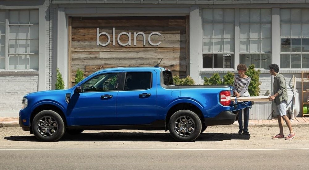 People unloading lumber from the bed of a blue 2024 Ford Maverick XLT in a trendy area.