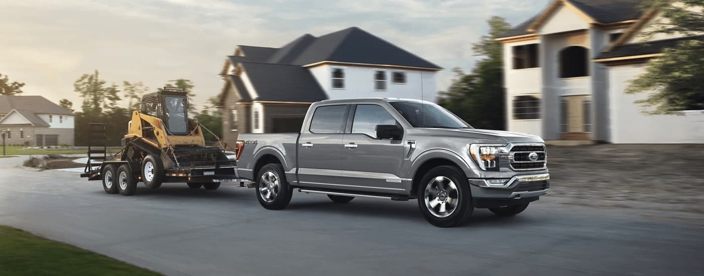 A silver 2023 Ford F-150 towing construction equimpent through a residential development.