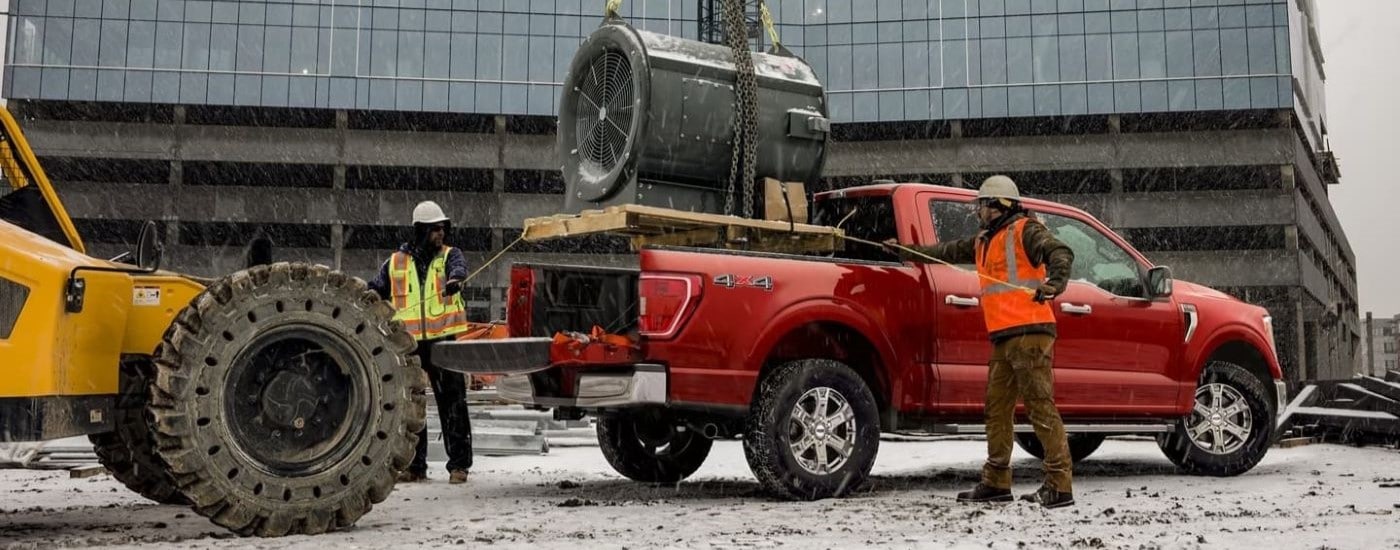 Construction workers loading a turbine into the bed of a red 2023 Ford F-150.