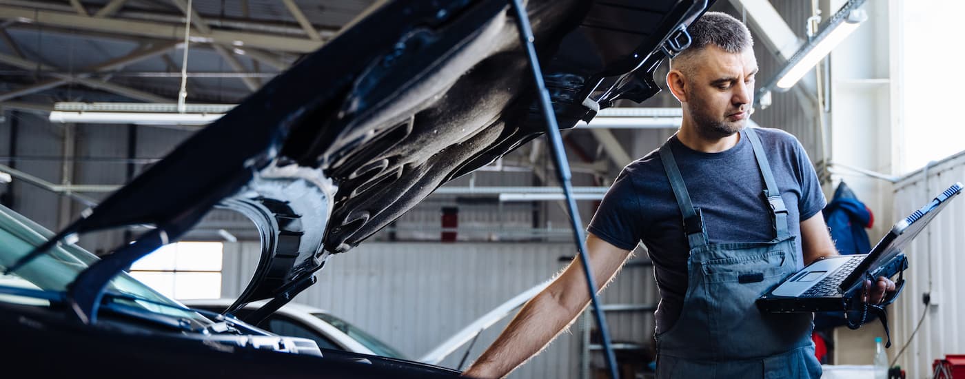 A mechanic is shown inspecting an engine while using a computer.