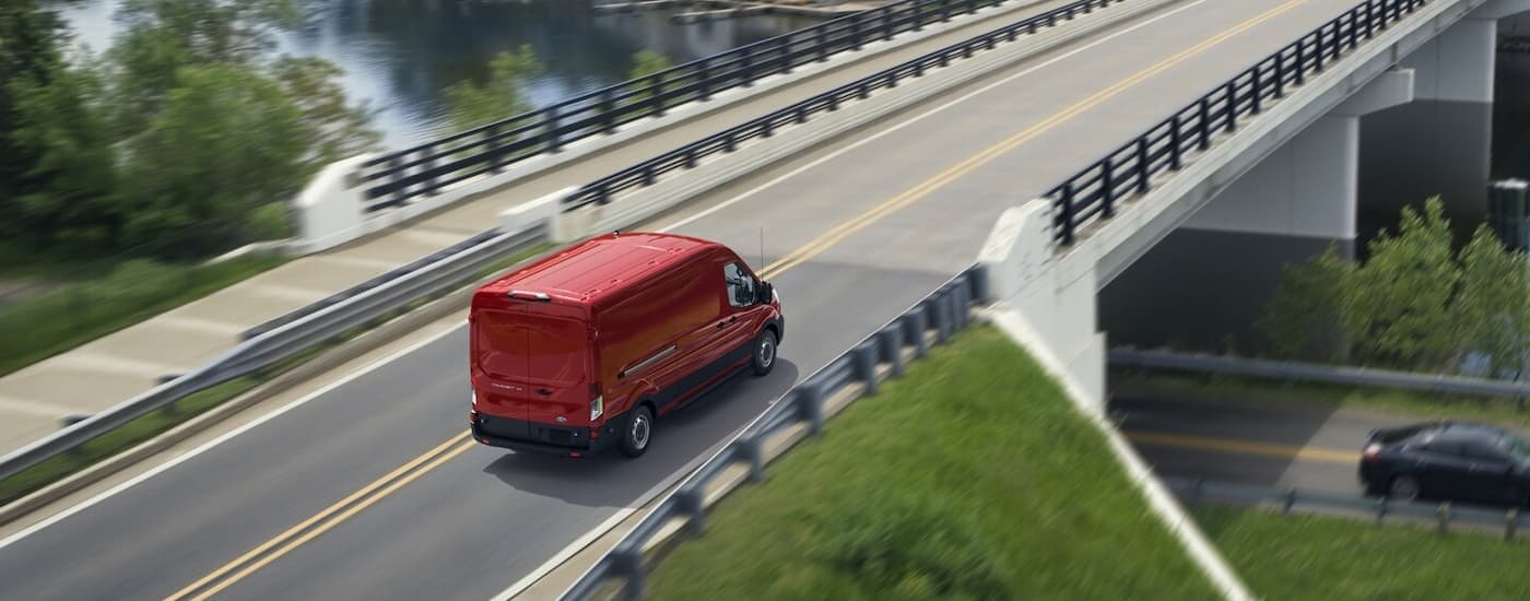 A red 2024 Ford Transit for sale driving on a bridge.