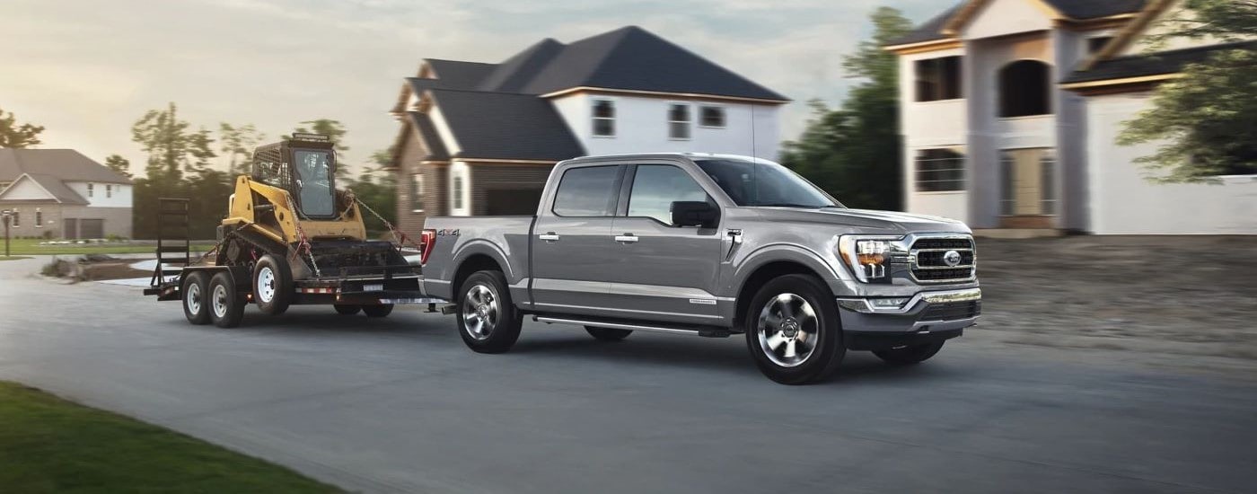 A grey 2023 Ford F-150 towing construction equipment through a residential development.