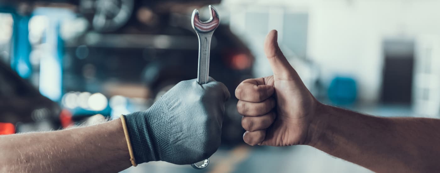 Gloved hand holding a wrench next to a thumbs up