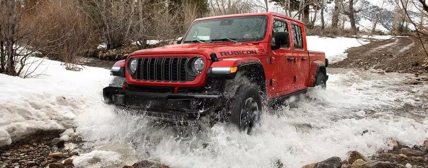 Red 2024 Jeep Gladiator crossing a river in the winter