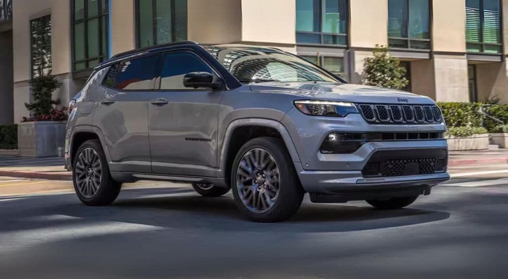 A grey 2024 Jeep Compass is shown driving on a city street after leaving a Jeep dealer.