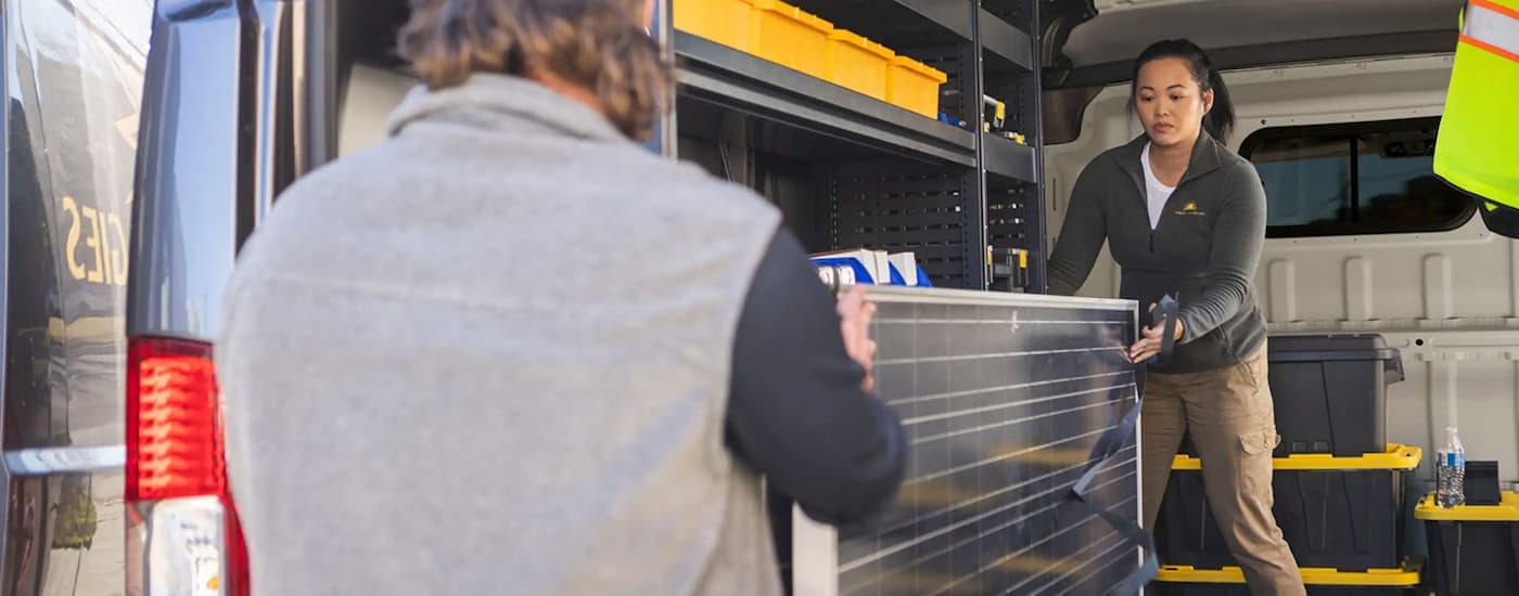 Two people are loading a panel into the back of a 2024 Ram ProMaster.