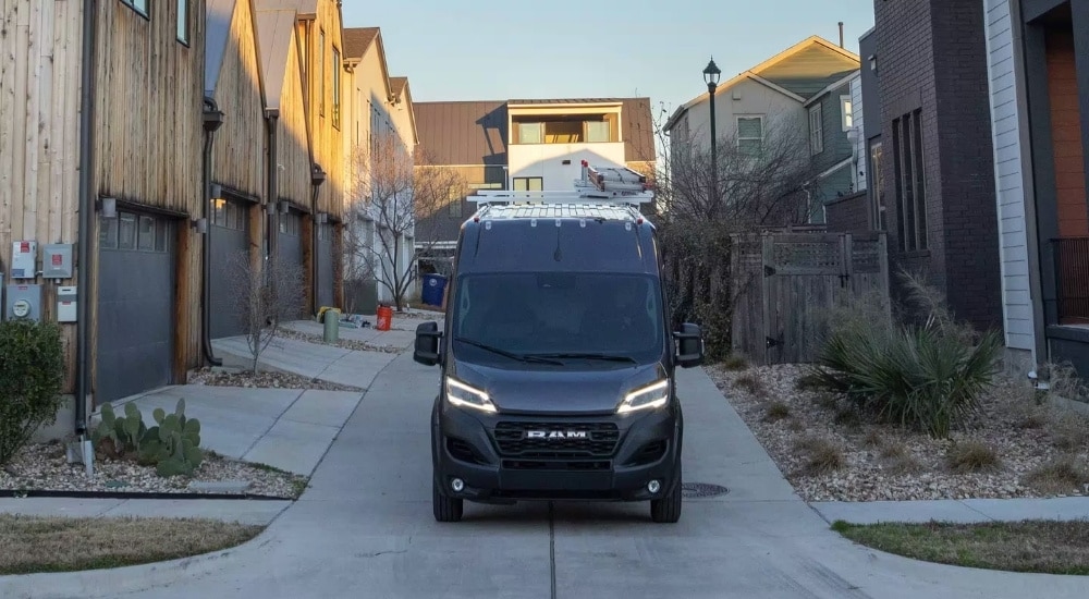 Head-on view of a grey 2024 Ram ProMaster for sale parked in a housing development.
