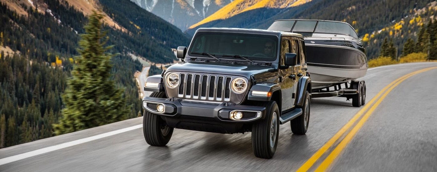 A grey 2023 Jeep Wrangler Unlimited it shown towing a boat.