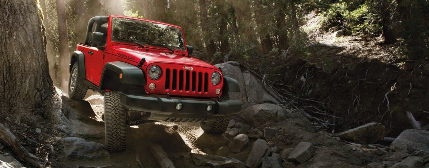 A red 2017 Jeep Wrangler Rubicon is shown off-roading in the woods.