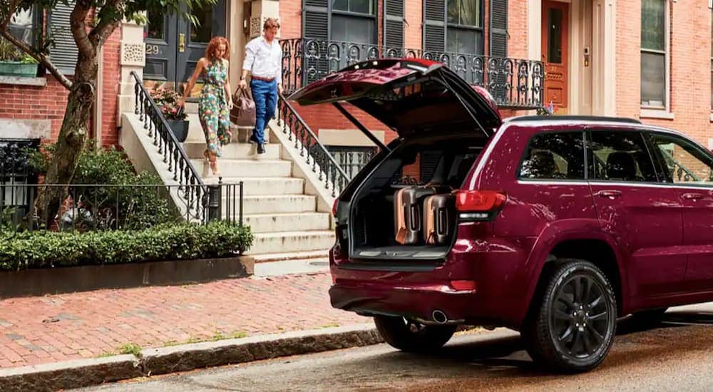 A red 2022 Jeep Grand Cherokee WK is parked on the side of a street with the rear storage door open.