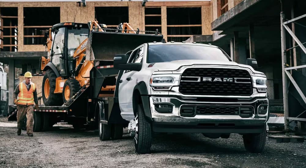A white 2024 Ram 5500 towing heavy machinery on a trailer.