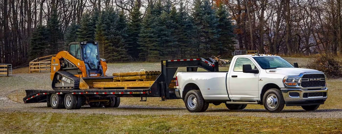 A white 2024 Ram 3500 Dually is shown from the side while towing a skid-steer.