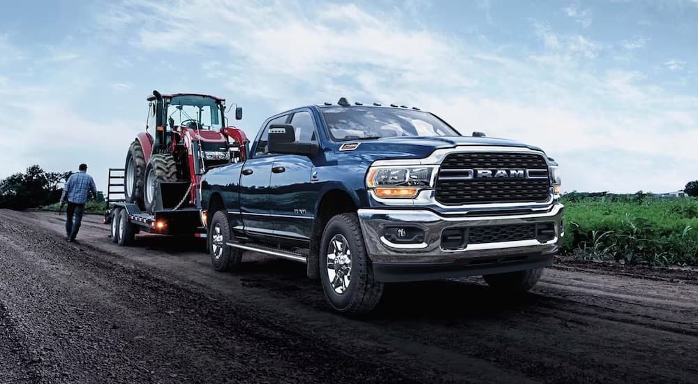 A blue 2024 Ram 2500 is shown towing a red tractor.