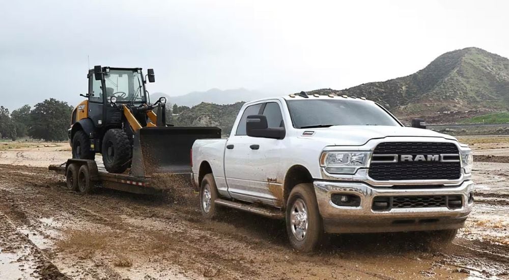 A white 2023 Ram 2500 Tradesman is shown towing construction equipment through mud.
