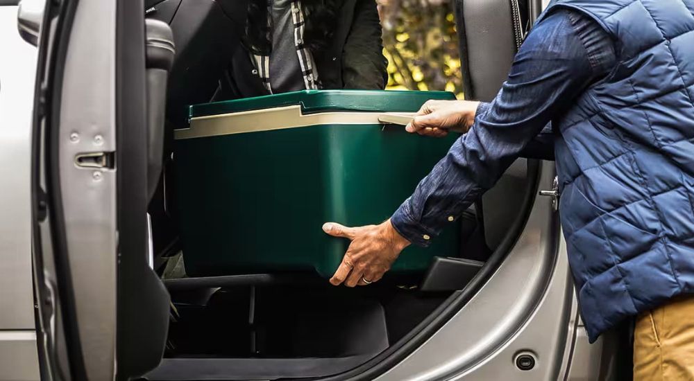 A person is shown stowing a green cooler in a white 2024 Ram 2500 for sale.