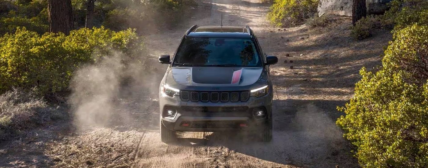 A grey 2023 Jeep Compass Trailhawk is shown kicking up dust on a trail.
