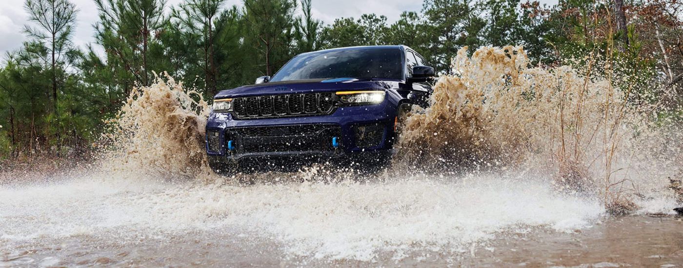 A dark blue 2024 Jeep Grand Cherokee 4xe is shown splashing through water after visiting a Jeep dealer.
