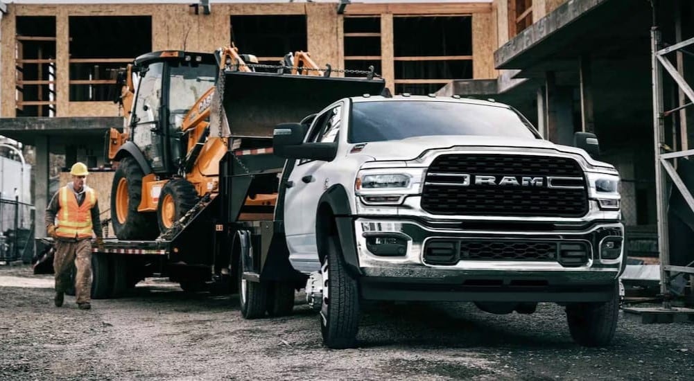 A white 2024 Ram Chassis Cab 5500 is shown towing construction equipment after looking at commercial vehicles for sale.