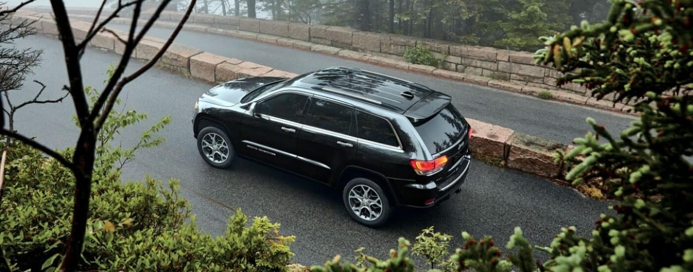 A popular used Jeep for sale, a grey 2021 Jeep Grand Cherokee, is shown on a mountain road.