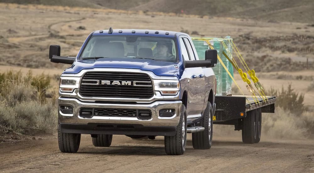 A blue 2021 Ram 2500 Big Horn is towing a trailer on a dirt road.