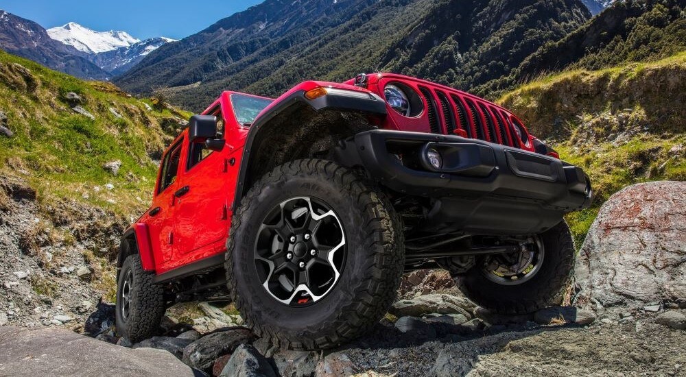 Close-up of the front wheel of a red 2023 Jeep Wrangler Unlimited off-roading over boulders.