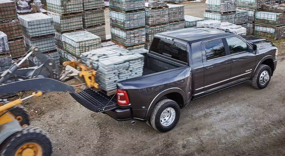 A construction vehicle loading a pallet into the bed of a black 2024 Ram 3500.