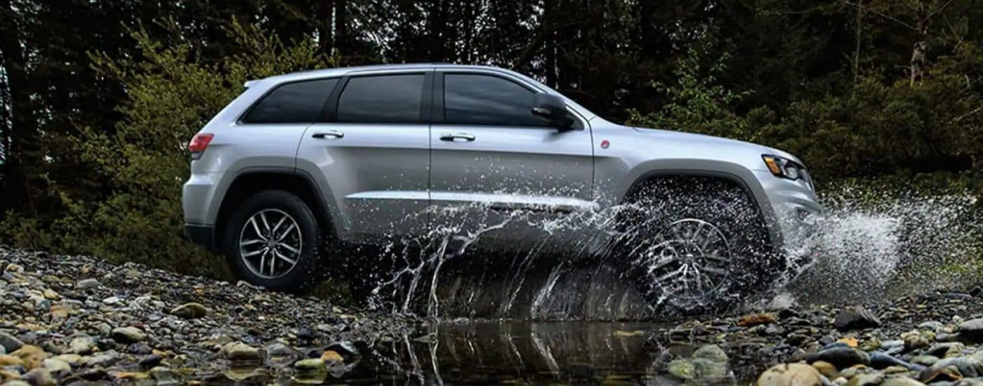 A silver 2020 Jeep Grand Cherokee is shown splashing through a creek.
