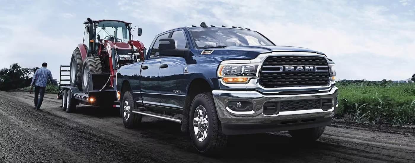 A blue 2024 Ram 2500 Laramie is shown towing a trailer off-road.