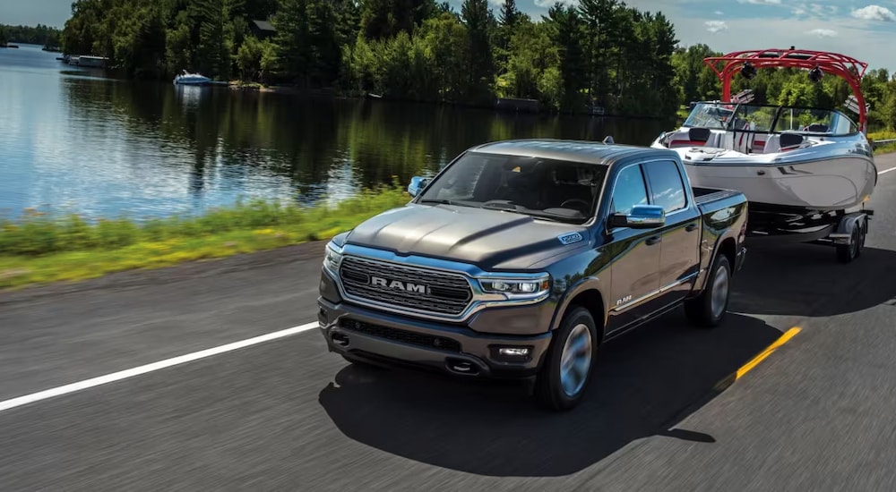 A grey 2023 Ram 1500 is towing a boat next to a lake.