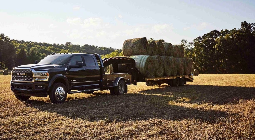 A black 2024 Ram 5500 Cassis Cab with Gooseneck Upfit towing bales of hay in a field.