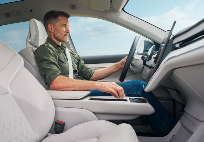 Low angle perspective shot of a man driving a Volvo EX90 while manipulating the infotainment dial.