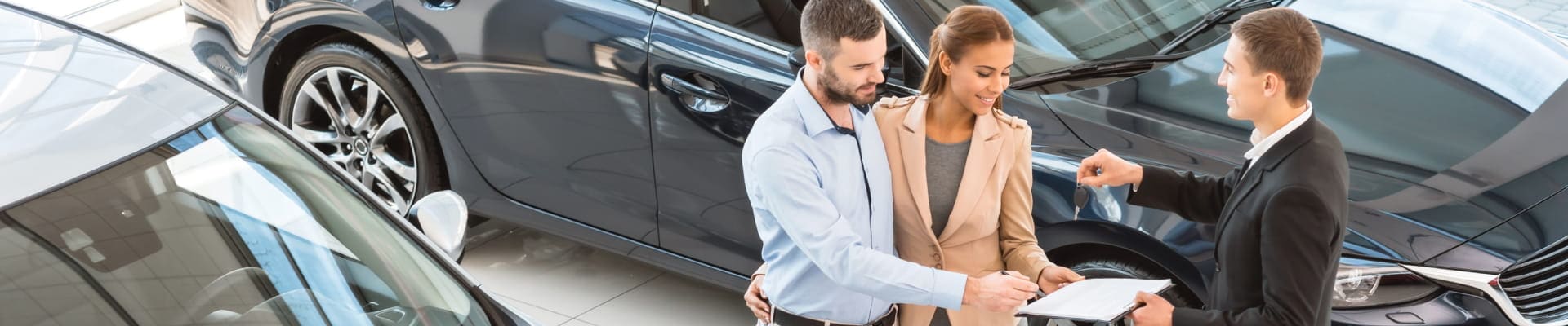 Couple receiving vehicle keys from a salesperson at a dealership.