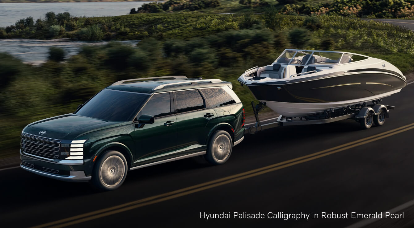 Hyundai Palisade towing a motorboat on a scenic lakeside highway.