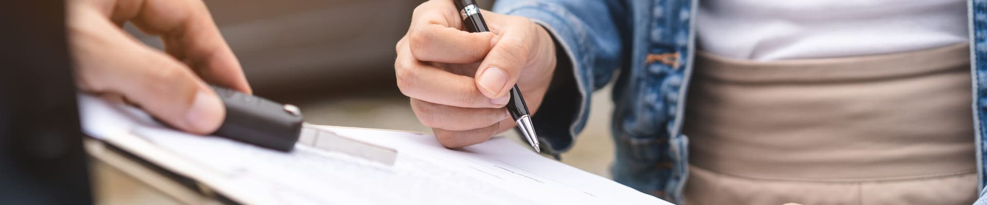 Customer signing paperwork on a clipboard while receiving assistance at a car dealership.