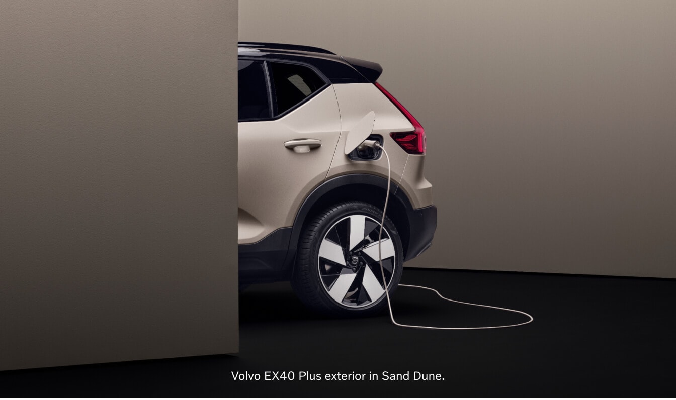 Rear three-quarter view of a Volvo EX40 Plus in Sand Dune charging via a cable in a studio environment.