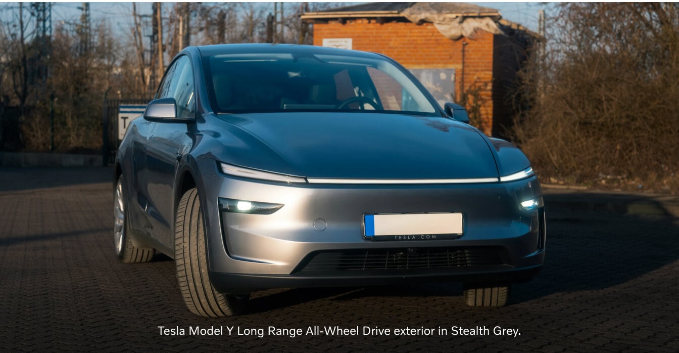 Three-quarter front view of a Stealth Grey Tesla Model Y parked on a cobblestone lot.