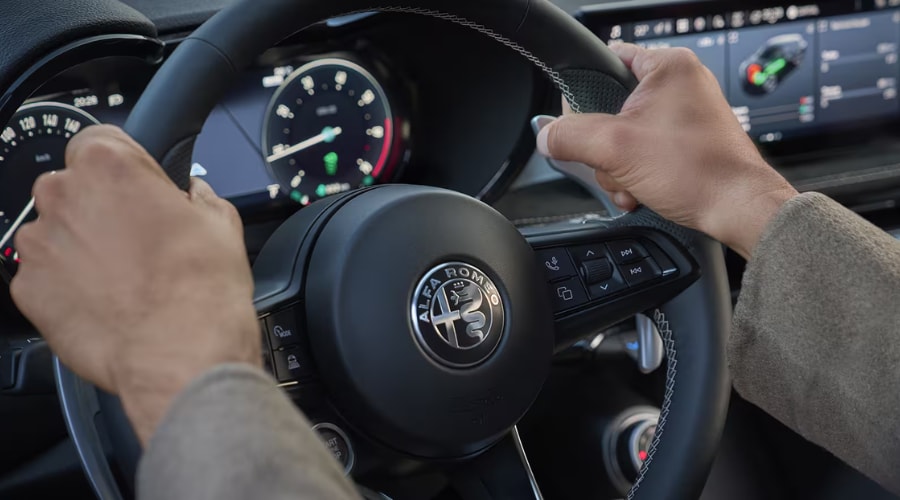 Driver holding the leather steering wheel inside a 2026 Alfa Romeo Tonale, showcasing the 12.3-inch Cannocchiale digital instrument cluster and 10.25-inch Uconnect touchscreen infotainment display for Route 17 commuters in Ramsey, NJ.