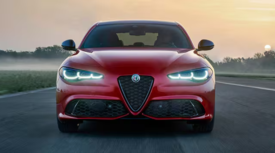 Front view of a red 2026 Alfa Romeo Giulia driving through early morning mist with illuminated Trilobe LED headlights on a highway near Ramsey, NJ