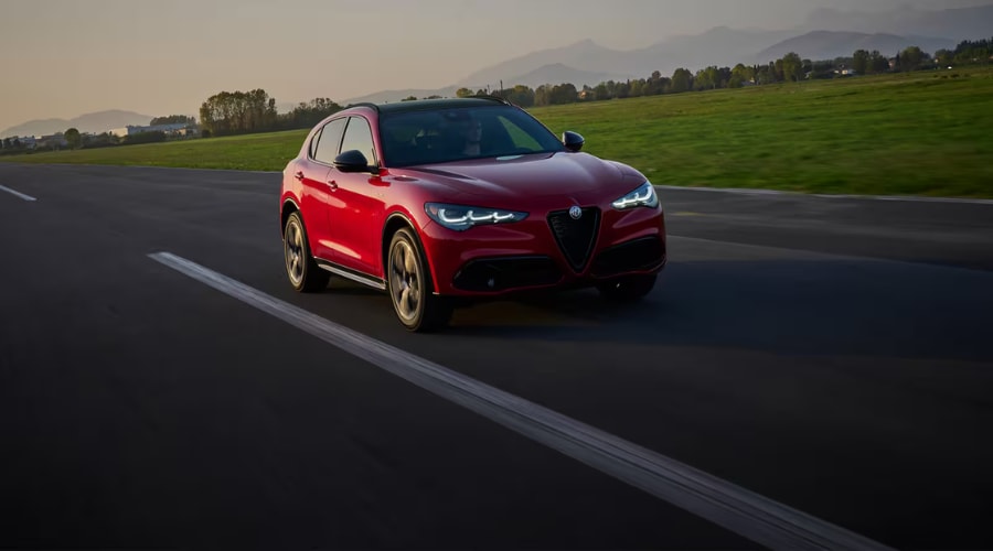 Front view of a red 2026 Alfa Romeo Stelvio accelerating at speed with active LED matrix headlights and race-bred Italian handling