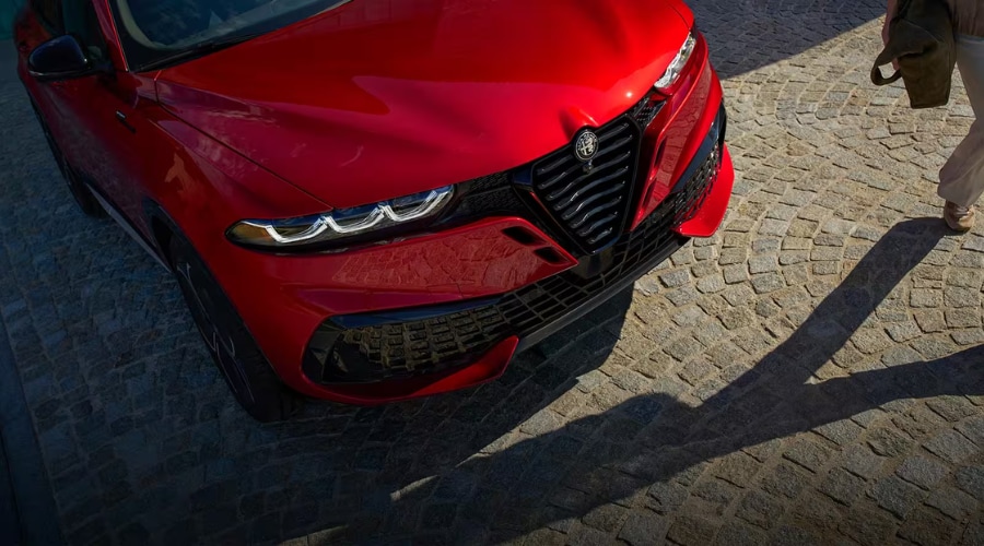 Front view of a red 2026 Alfa Romeo Tonale showing the iconic Scudetto V-shield grille, integrated front radar sensor emblem, and 3+3 LED matrix headlights parked in Bergen County, NJ.