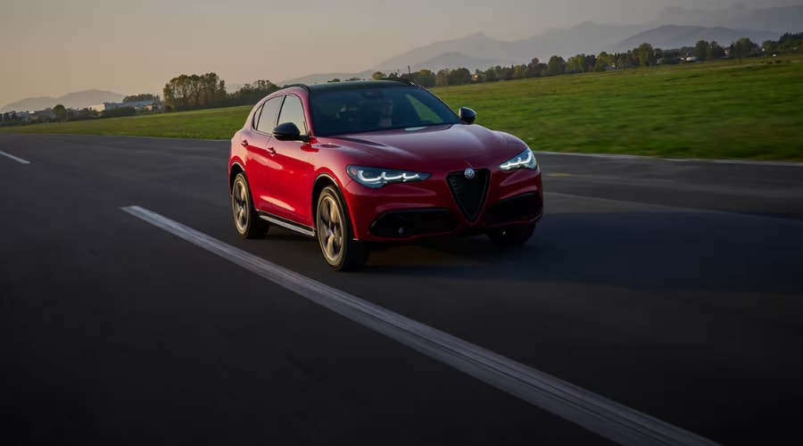 Front three-quarter view of a red 2026 Alfa Romeo Stelvio driving at sunset, showcasing full LED matrix headlights and iconic Scudetto grille near Ramsey Alfa Romeo in Bergen County, NJ