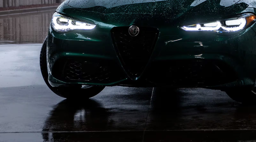 Low-angle front view of a rain-covered Verde Montreal green 2026 Alfa Romeo Giulia AWD luxury sports sedan on wet pavement, displaying illuminated 