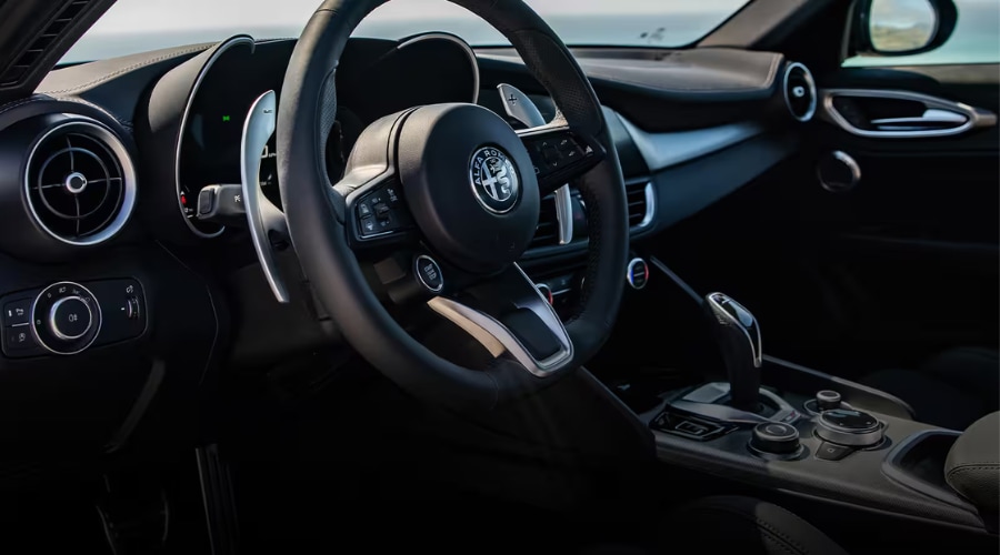 Interior cockpit view of a 2026 Alfa Romeo Giulia luxury sports sedan featuring a black leather-wrapped steering wheel with integrated start/stop button, large column-mounted aluminum paddle shifters, binocular digital instrument cluster, and turbine-style air vents, delivering ergonomic daily commuter comfort for Route 17 drivers in Bergen County, NJ.